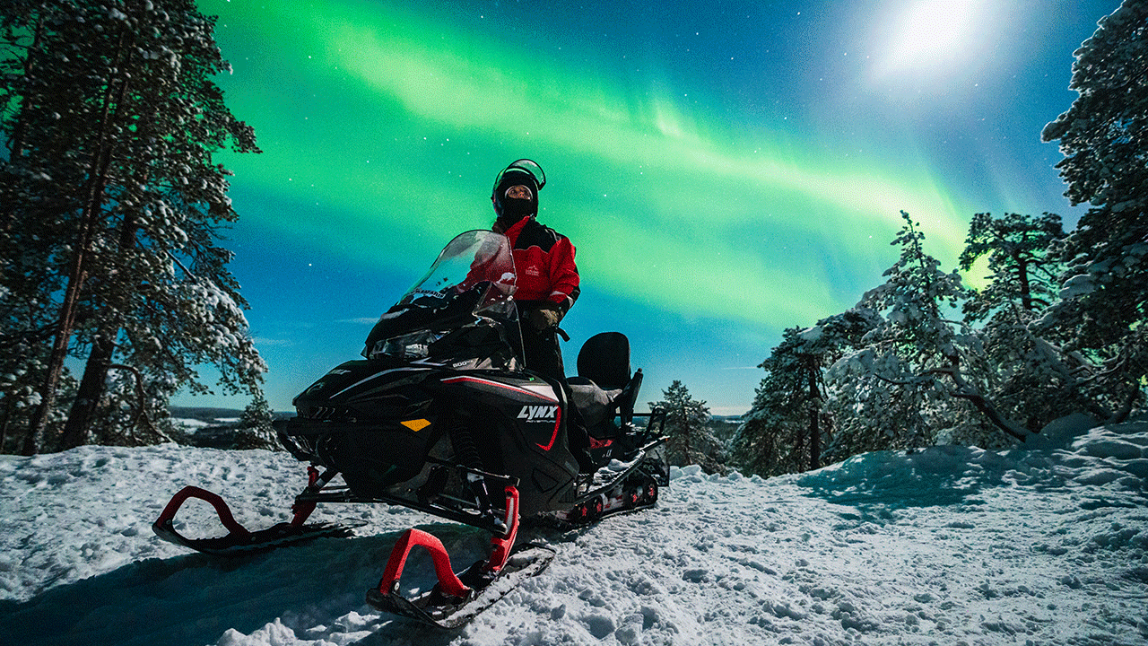 Mies ajaa moottorikelkalla ja taustalla ovat revontulet